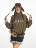 Woman wearing a green graphic print sweatshirt and black denim skirt with fur trim, holding her hat ear flaps.