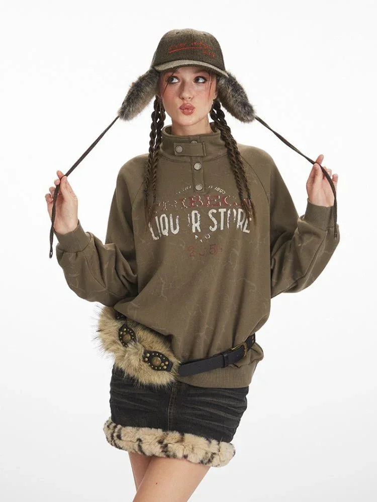 Woman wearing a green graphic print sweatshirt and black denim skirt with fur trim, holding her hat ear flaps.