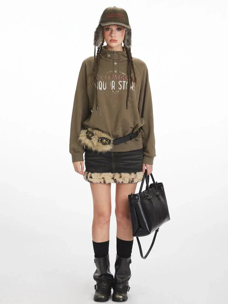 Woman wearing a green graphic print sweatshirt with a collared button placket, black denim skirt with fur trim, black boots, and a black handbag.