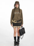 Woman wearing a green graphic print sweatshirt with a collared button placket, black denim skirt with fur trim, black boots, and a black handbag.