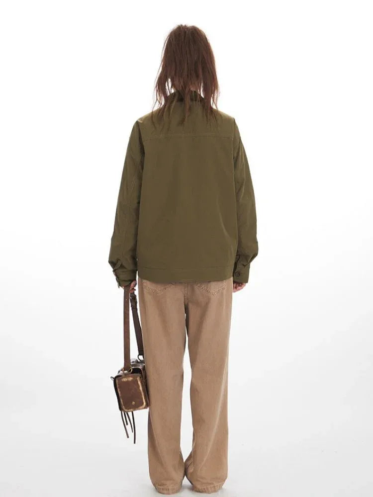 Rear view of a woman in an olive green jacket with a brown collar and tan wide-leg pants, holding a brown crossbody bag.