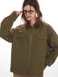 Detail shot of the sleeve and chest pocket of an olive green jacket with a brown collar, showing a label.