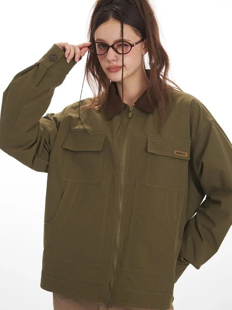 Detail shot of the sleeve and chest pocket of an olive green jacket with a brown collar, showing a label.