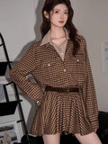 Woman wearing a brown plaid button-down shirt dress with a collared neckline and a belted waist