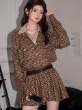 Woman holding a phone while wearing the brown plaid shirt dress