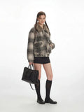 Side view of a woman in a plaid bomber jacket with a fur collar, holding a black handbag.