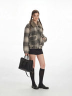 Side view of a woman in a plaid bomber jacket with a fur collar, holding a black handbag.