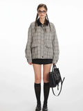 Woman wearing a grey plaid bomber jacket with a black collar, black shorts, black knee-high socks, and black shoes, holding a black handbag.