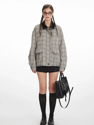 Woman wearing a grey plaid bomber jacket with a black collar, black shorts, black knee-high socks, and black shoes, holding a black handbag.
