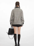 Back view of a woman wearing a grey plaid bomber jacket with a black collar, black shorts, black knee-high socks, and black shoes, holding a black handbag.