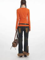 Back view of a woman wearing an orange long-sleeve notch neck top, dark wash distressed jeans with cargo pockets and fur trim cuffs, and a brown crossbody bag.