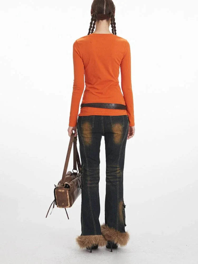 Back view of a woman wearing an orange long-sleeve notch neck top, dark wash distressed jeans with cargo pockets and fur trim cuffs, and a brown crossbody bag.