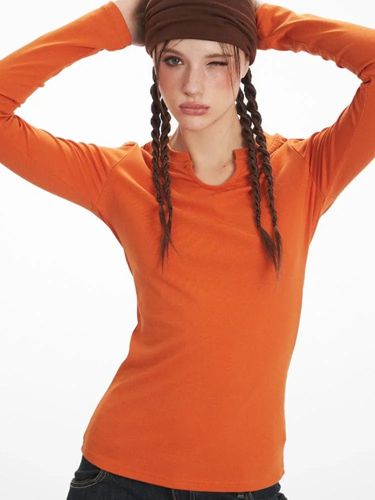 Close-up of a woman wearing an orange long-sleeve notch neck top and a brown headband, winking.