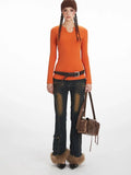 Woman wearing an orange long-sleeve notch neck top, dark wash distressed jeans with cargo pockets and fur trim cuffs, a brown belt, and a brown crossbody bag.