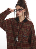 Close-up of a woman wearing a red and tan plaid hooded flannel shirt and oval-shaped glasses.