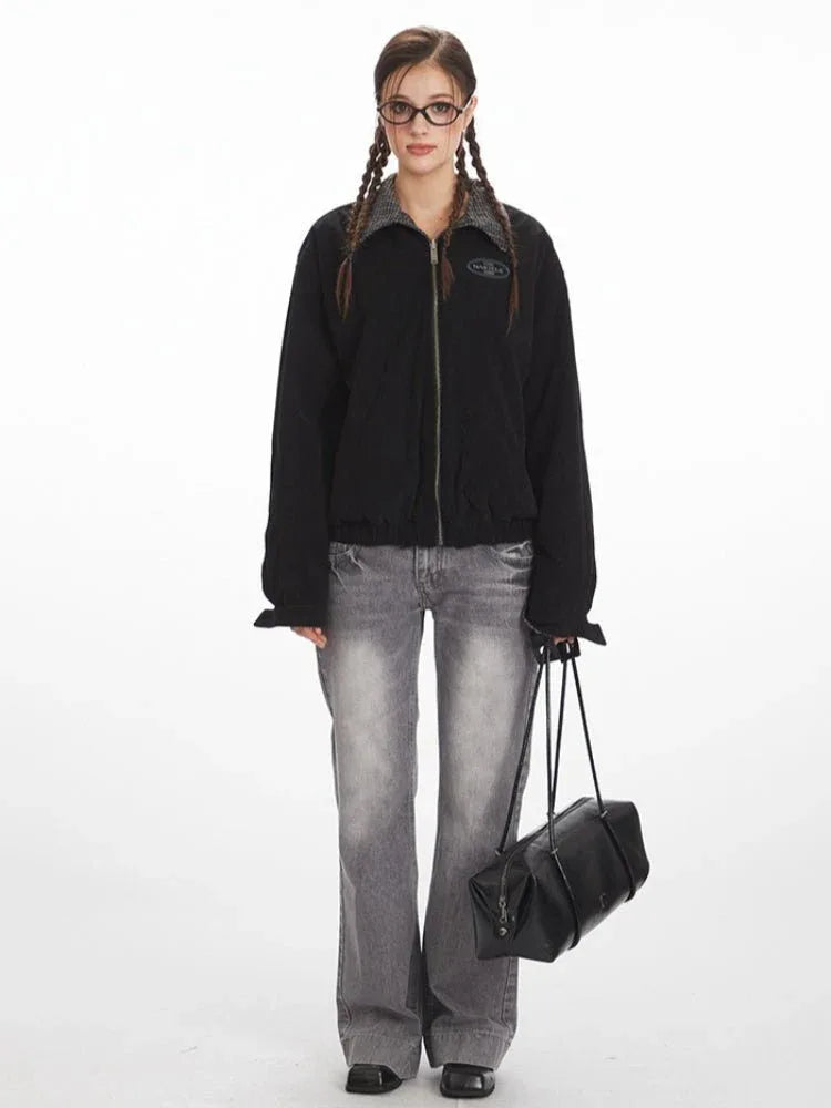 Woman wearing a black bomber jacket with a grey plaid collar and cuffs, paired with grey wide-leg jeans.