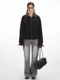 Woman wearing a black bomber jacket with a grey plaid collar and cuffs, paired with grey wide-leg jeans.