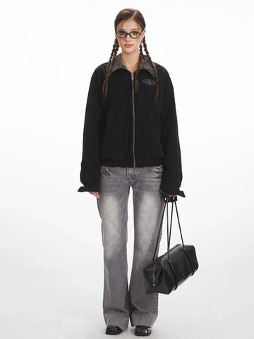Woman wearing a black bomber jacket with a grey plaid collar and cuffs, paired with grey wide-leg jeans.