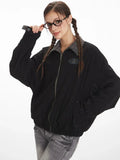 Woman adjusting her glasses while wearing a black bomber jacket with a grey plaid collar and cuffs.
