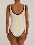 Back view of a woman wearing a cream ribbed knit one-piece swimsuit with black trim.