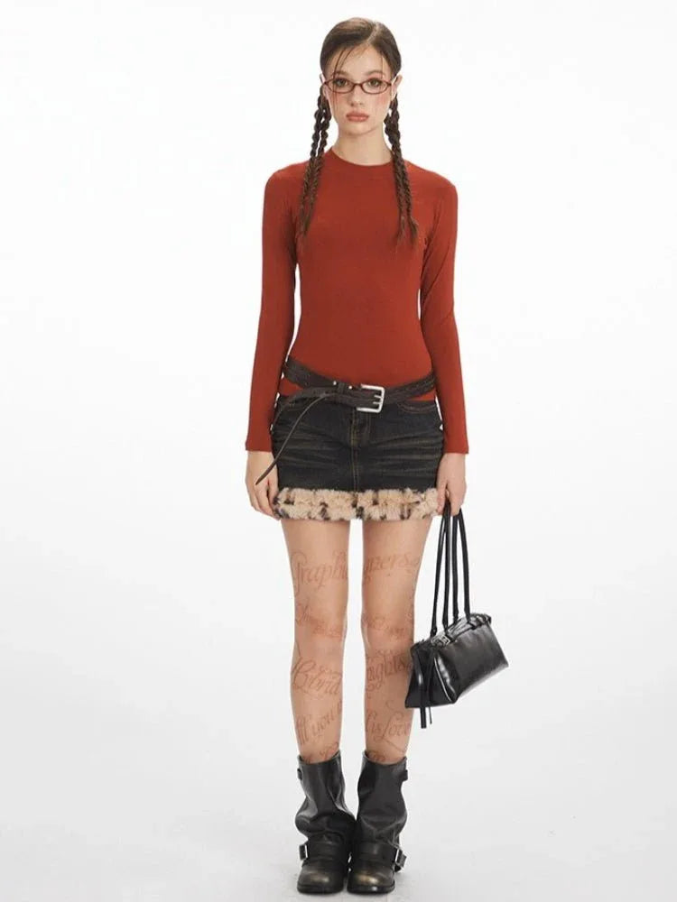 Model wearing a rust-colored long-sleeve top and a dark wash denim mini skirt with faux fur trim.