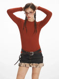 Front view of a model with braided pigtails, wearing a rust-colored long-sleeve top and a denim mini skirt with faux fur trim, hands on head.