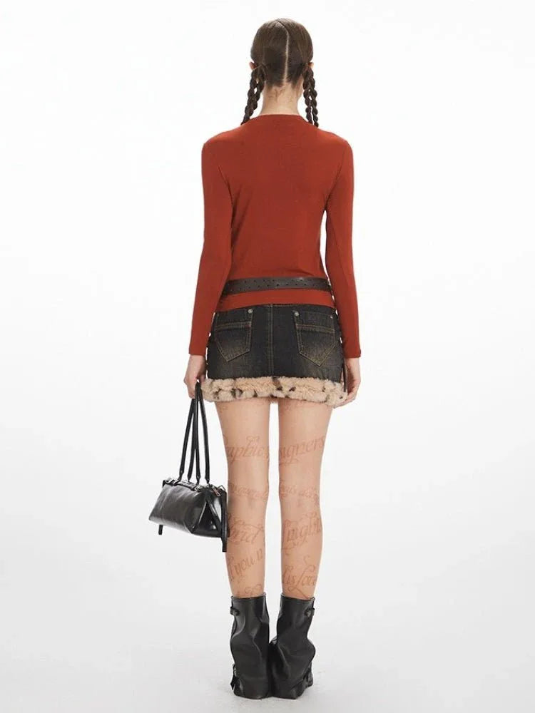 Model wearing a rust-colored long-sleeve top and a dark wash denim mini skirt with faux fur trim.