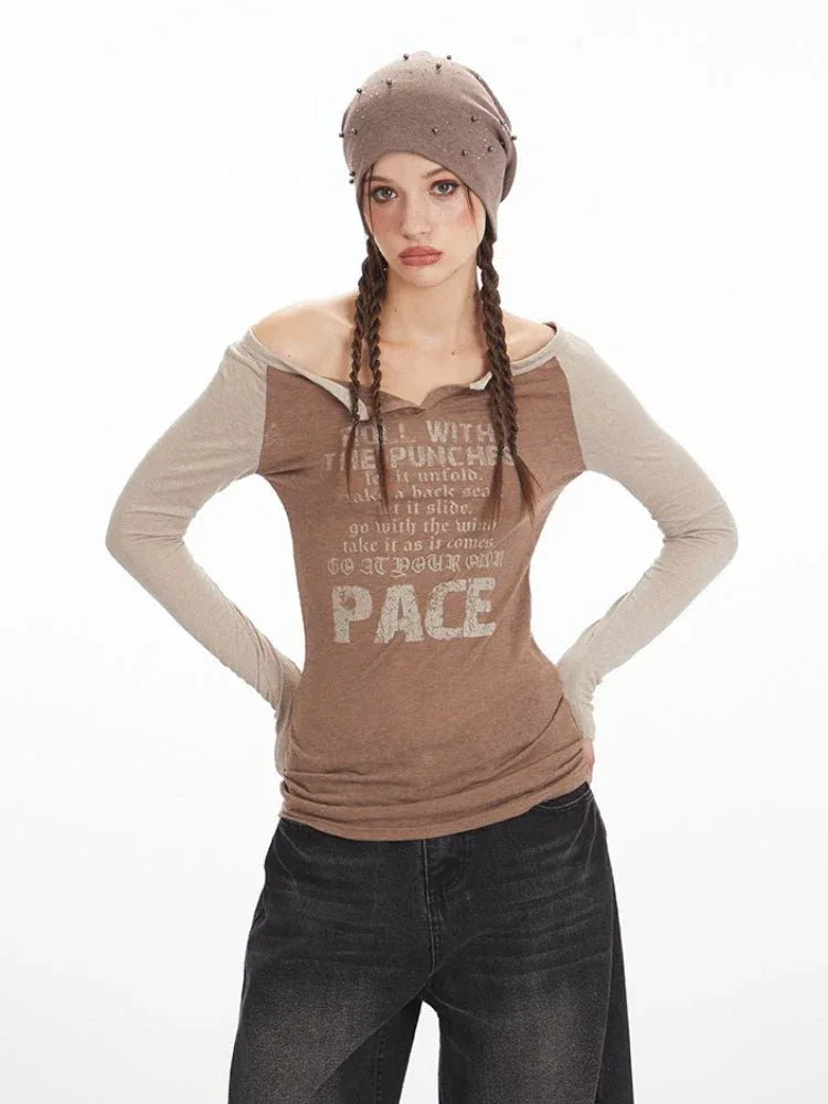 Woman in a brown long-sleeve graphic t-shirt with beige sleeves, dark wash wide-leg jeans, and a brown beret, posing with hands on hips.