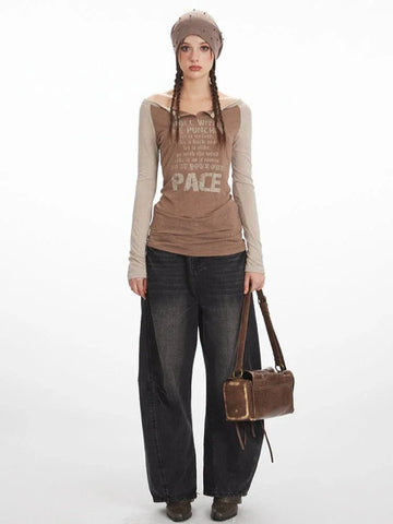 Woman wearing a brown long-sleeve graphic t-shirt with contrasting beige sleeves, dark wash wide-leg jeans, and a brown beret.