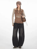 Full body shot of a woman wearing a brown long-sleeve graphic t-shirt with beige sleeves, dark wash wide-leg jeans, a brown beret, and a brown crossbody bag.