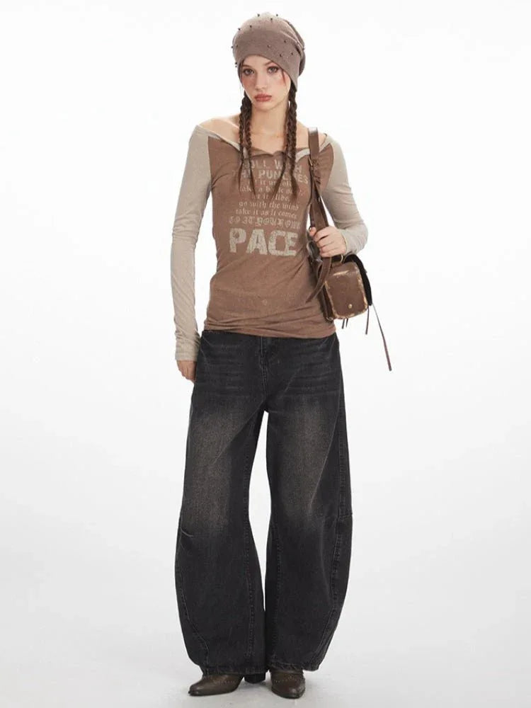 Full body shot of a woman wearing a brown long-sleeve graphic t-shirt with beige sleeves, dark wash wide-leg jeans, a brown beret, and a brown crossbody bag.
