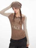 Close-up of a woman wearing a brown long-sleeve graphic t-shirt with beige sleeves, dark wash wide-leg jeans, and a brown beret.