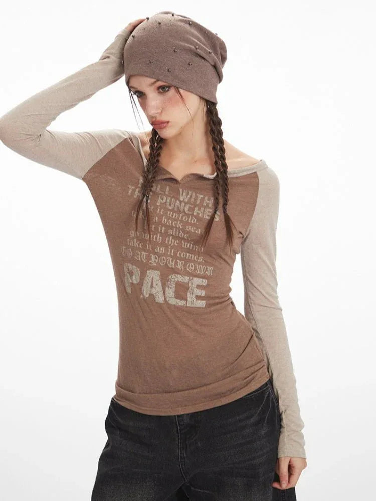 Close-up of a woman wearing a brown long-sleeve graphic t-shirt with beige sleeves, dark wash wide-leg jeans, and a brown beret.
