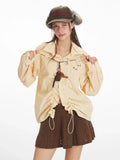 Woman wearing a yellow and white striped long-sleeved collared shirt with ruched drawstring detail and a brown knit skirt, adjusting the drawstring.