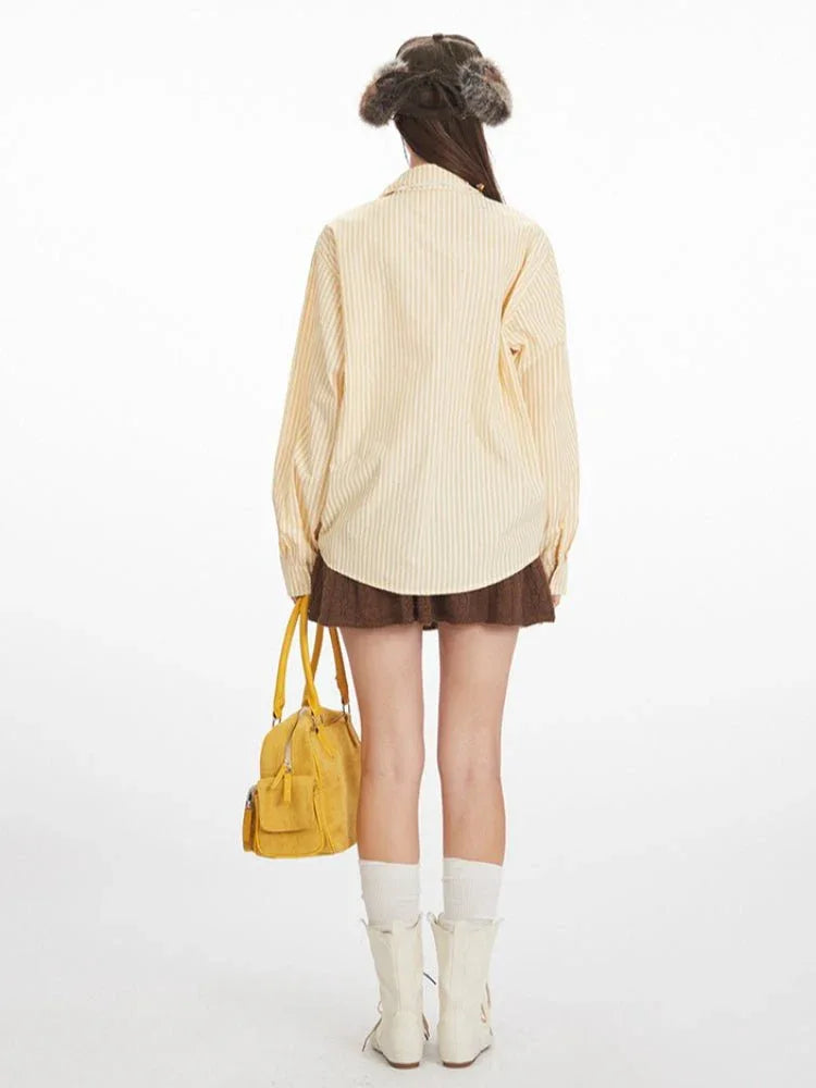 Woman wearing a yellow and white striped long-sleeved collared shirt with ruched drawstring detail, a brown knit skirt, white socks, and white boots, holding a yellow handbag.
