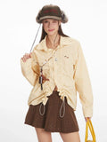 Woman wearing a yellow and white striped long-sleeved collared shirt with ruched drawstring detail and a brown knit skirt, winking and holding the drawstring.