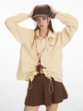 Woman wearing a yellow and white striped long-sleeved collared shirt with ruched drawstring detail and a brown knit skirt, wearing a hat and adjusting it.