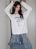 Model wearing a white long sleeve t-shirt with a graphic print, hands raised to her hair.