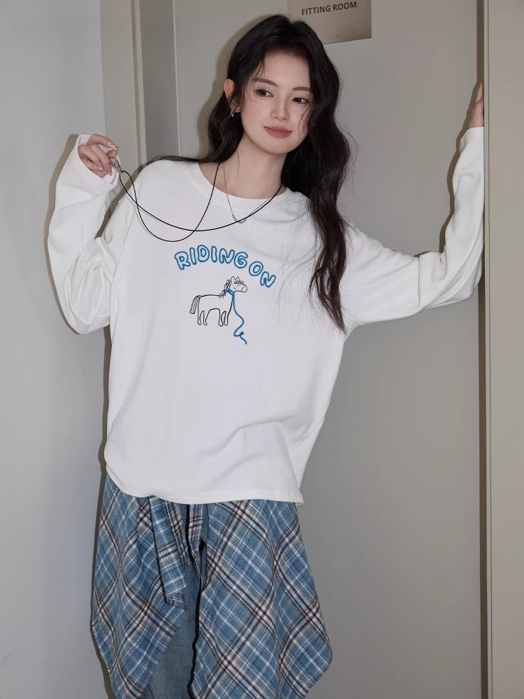 Woman posing in a white long sleeve graphic t-shirt and jeans, with a plaid shirt around her waist.