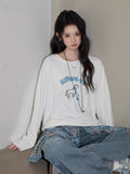 Model wearing a white long sleeve t-shirt with a blue horse graphic and text 'RIDING ON', paired with blue jeans and a plaid shirt tied around the waist.