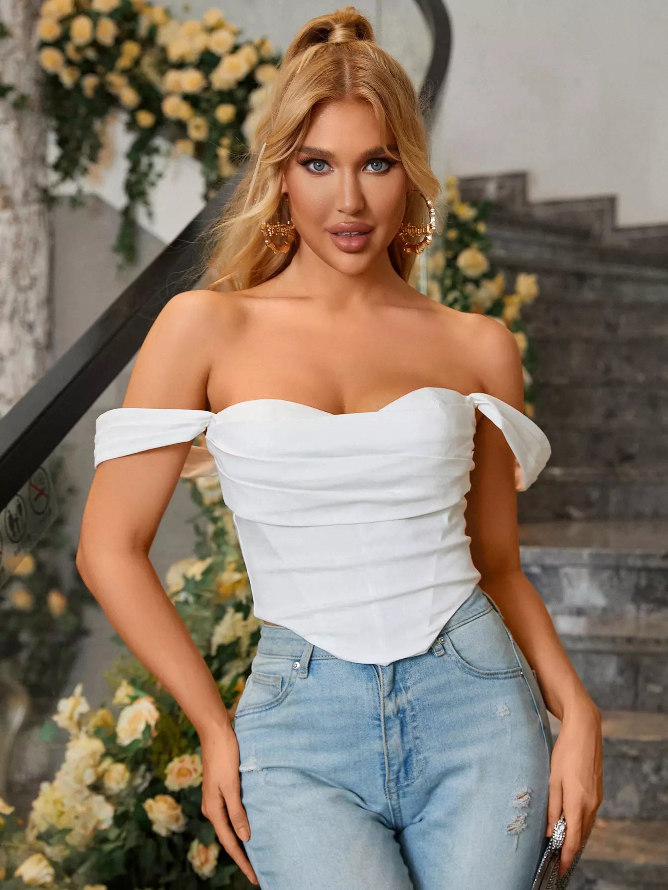 Close-up front view of a woman wearing a white off-the-shoulder ruched crepe top with a sweetheart neckline and light wash jeans.