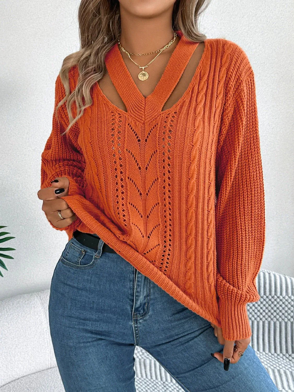 Woman wearing an orange long-sleeve knit sweater with a cut-out V-neck and cable knit details.