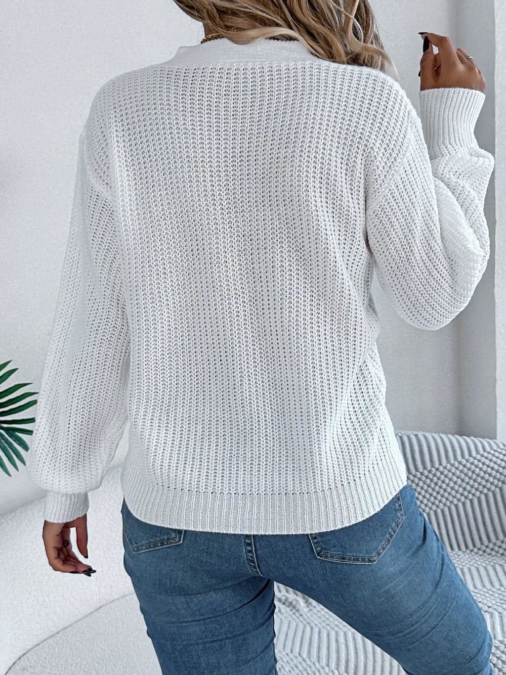 Back view of a woman in a white long-sleeve knit sweater.