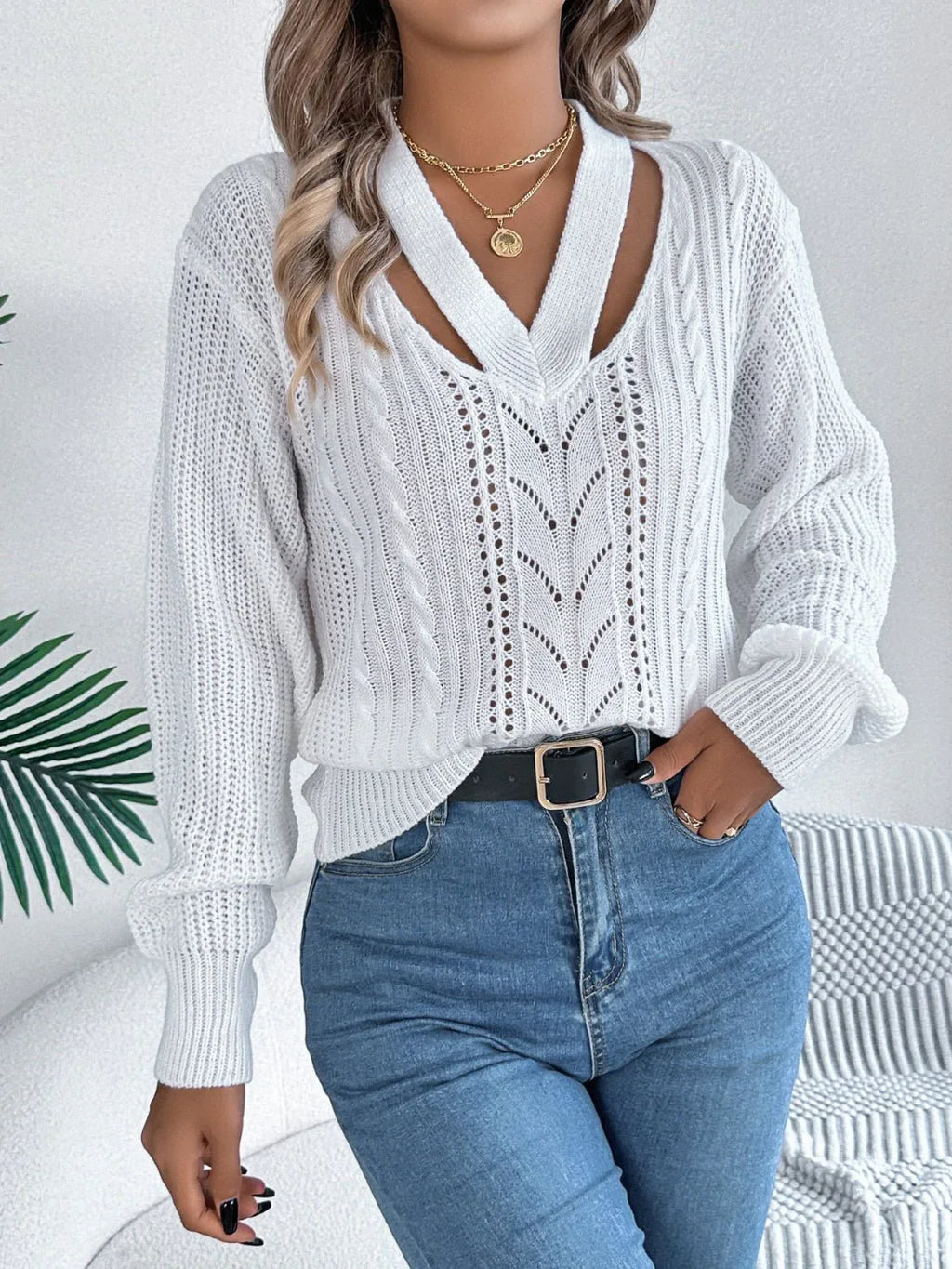 Front view of a woman wearing a white knit sweater with a cut-out V-neck and blue jeans.