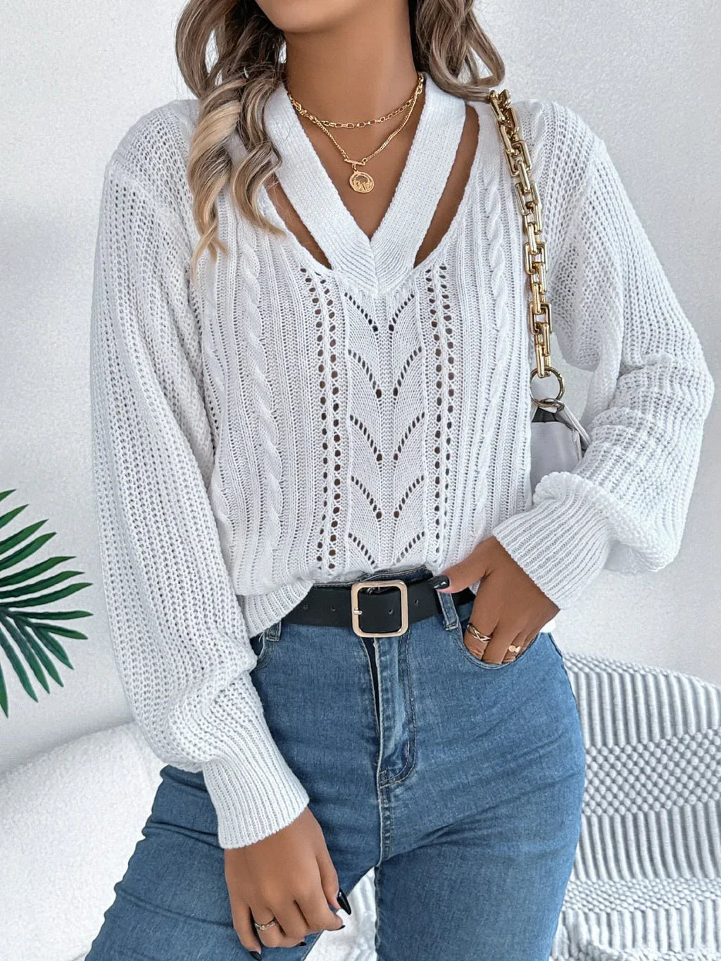 Woman in a white knit sweater with a cut-out V-neck and blue jeans, holding a handbag.