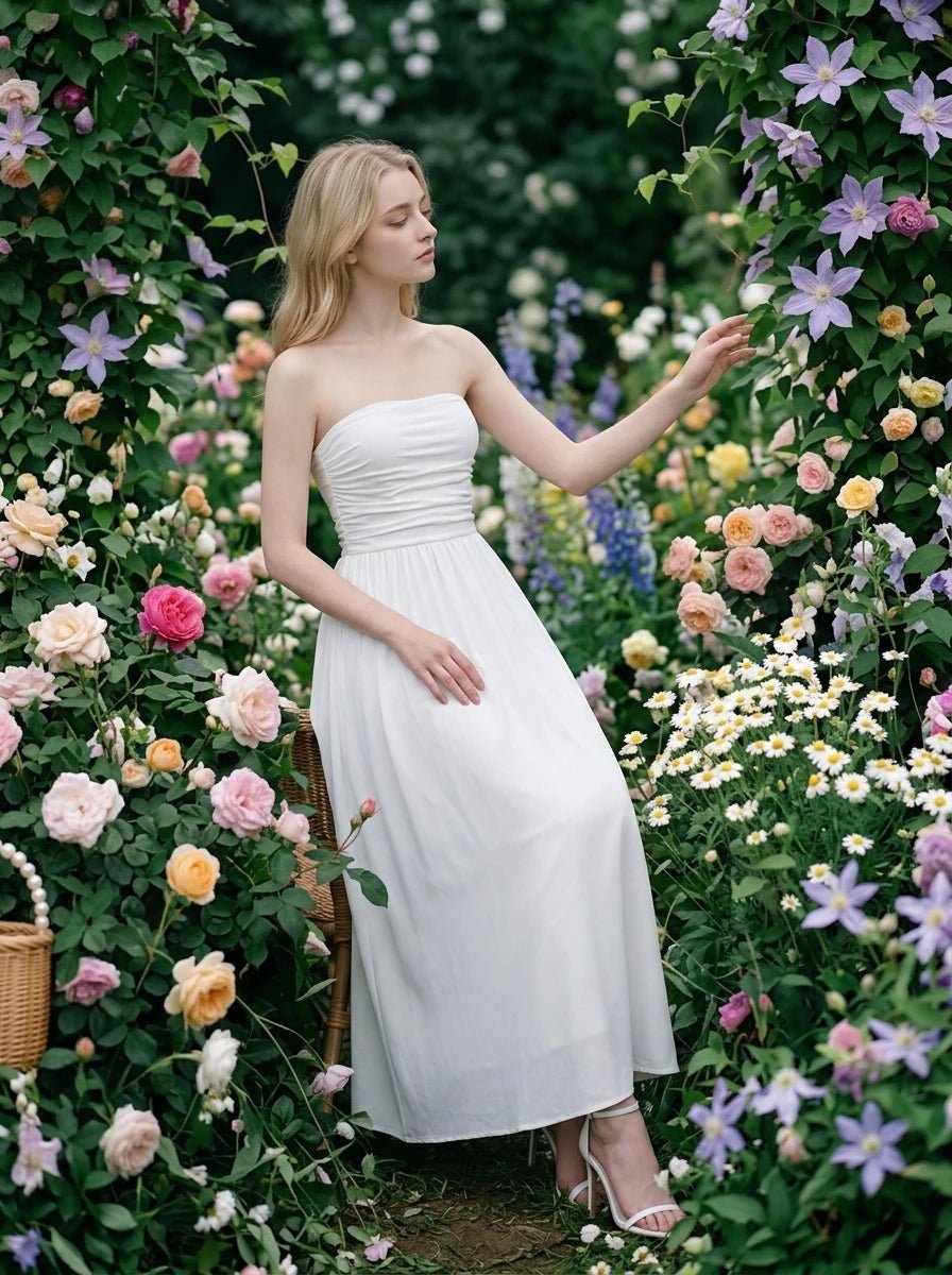 Woman wearing a white strapless ruched waist maxi dress sitting amongst flowers