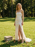 Woman wearing a white strapless satin gown with a high slit standing in a grassy park
