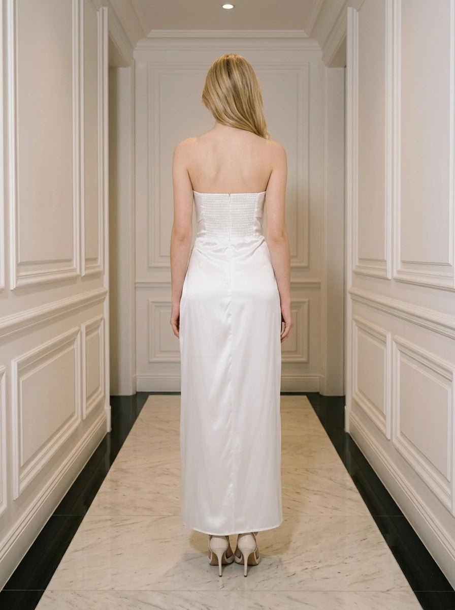 Woman wearing a white strapless satin gown with a high slit standing in a hallway