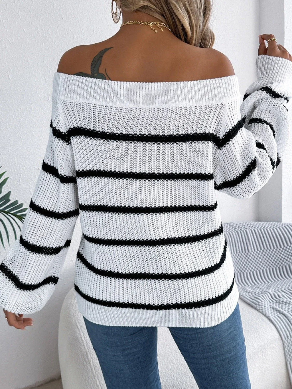 Back view of a woman wearing a white and black striped off-the-shoulder knit sweater with blue jeans