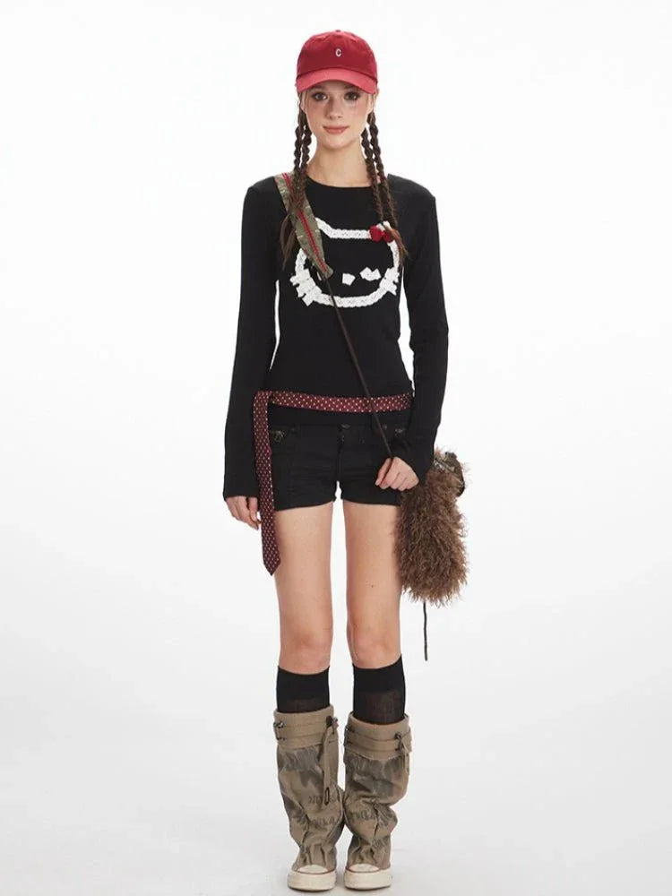 Woman wearing a black long-sleeved shirt with a white graphic print of a cat's face, black shorts, a red baseball cap, and camouflage boots.